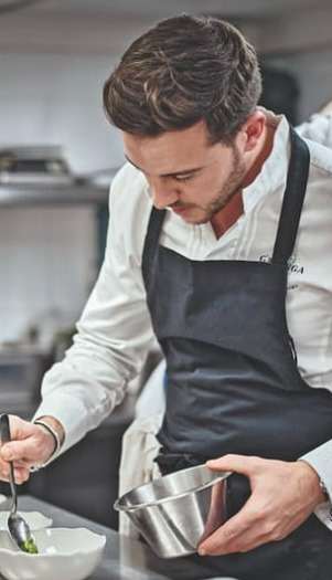 Le chef Thomas Danigo, en tablier noir, dresse une assiette en cuisine.