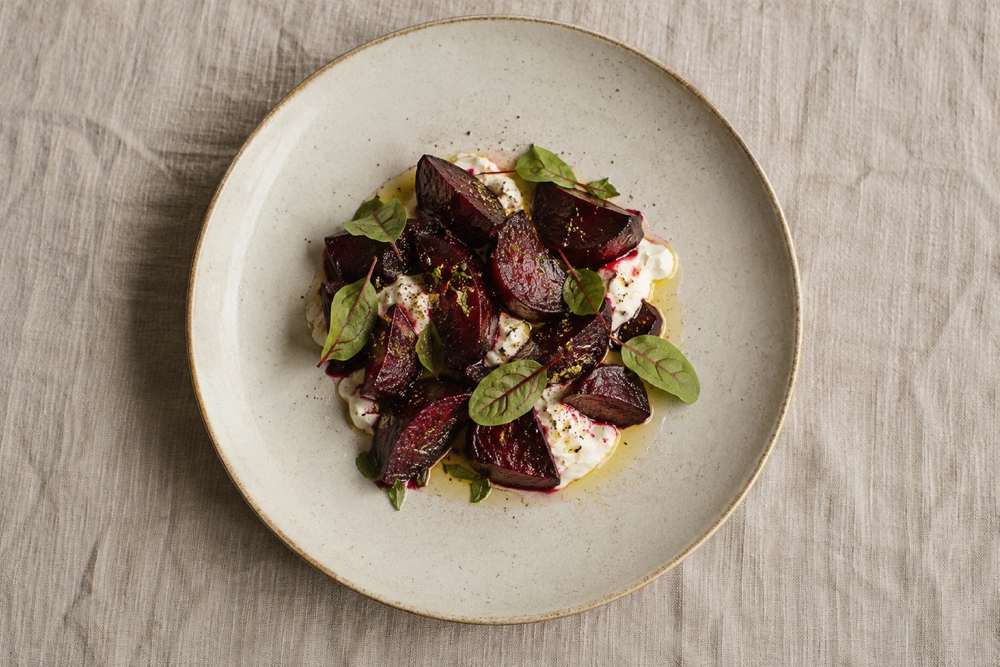 Betteraves rôties, crème et feuilles d’oseille dans une assiette en céramique sur lin naturel.